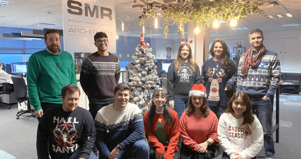 Team altogether in christmas jumpers in front of office christmas tree 